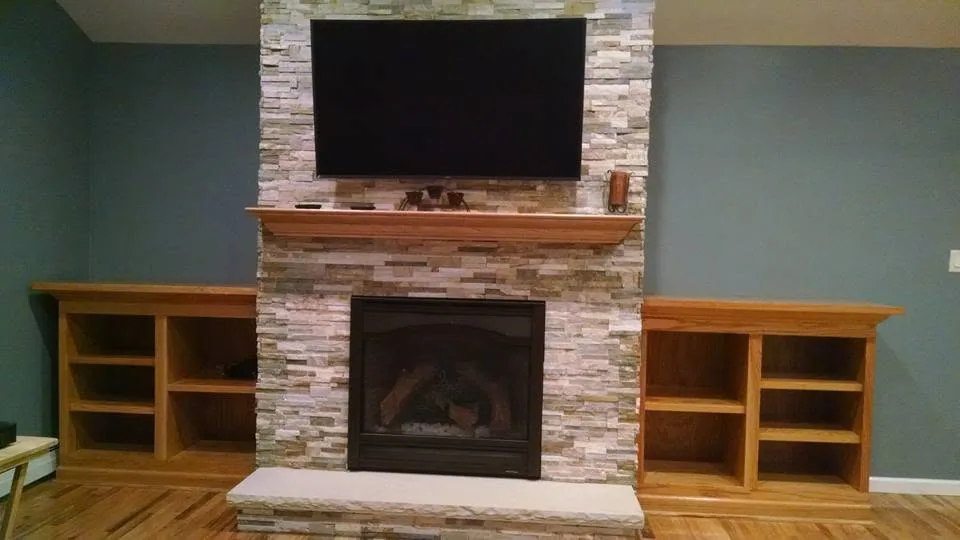 Stacked-stone fireplace flanked by custom oak built-ins by North South Construction
