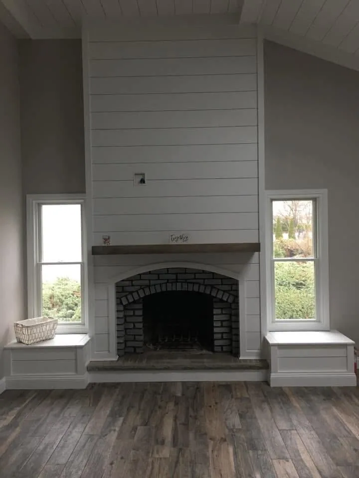 Floor-to-ceiling shiplap fireplace with brick arch and window seats by North South Construction